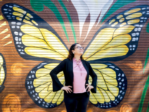 Anyi Mazo-Vargas in gront of butterfly wings mural